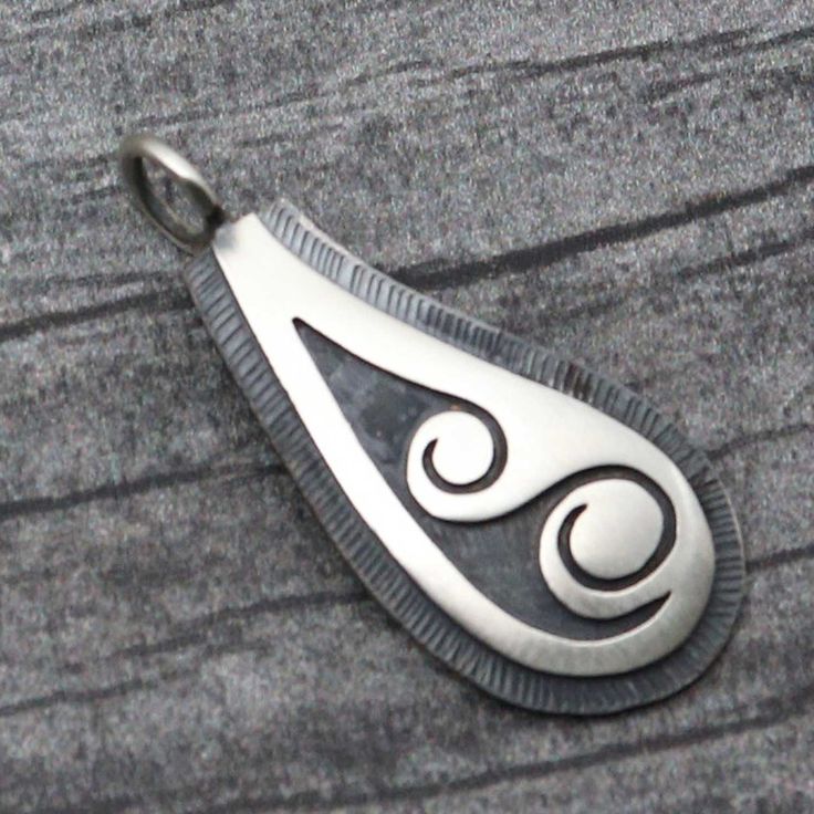 a silver pendant with an intricate design on it's side sitting on a piece of wood