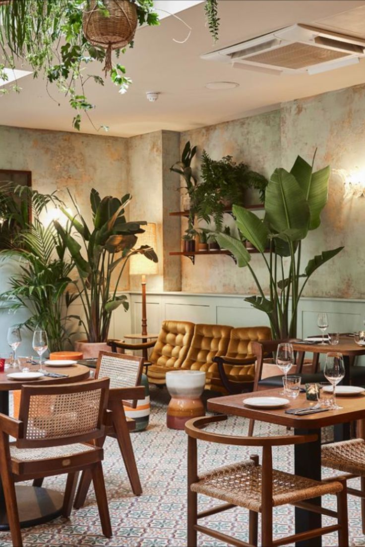 the interior of a restaurant with tables, chairs and potted plants on the wall