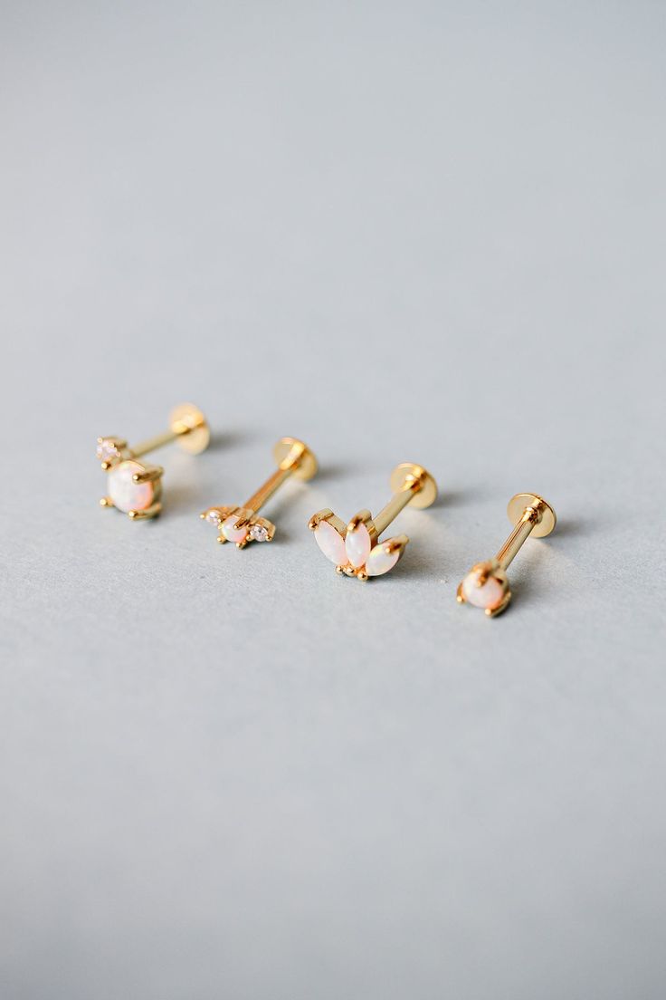 three pairs of gold earrings with white and pink flowers in them on a gray surface