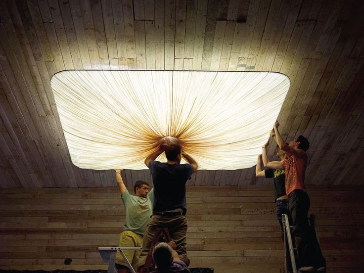 three men working on a large light fixture in a room with wooden walls and flooring