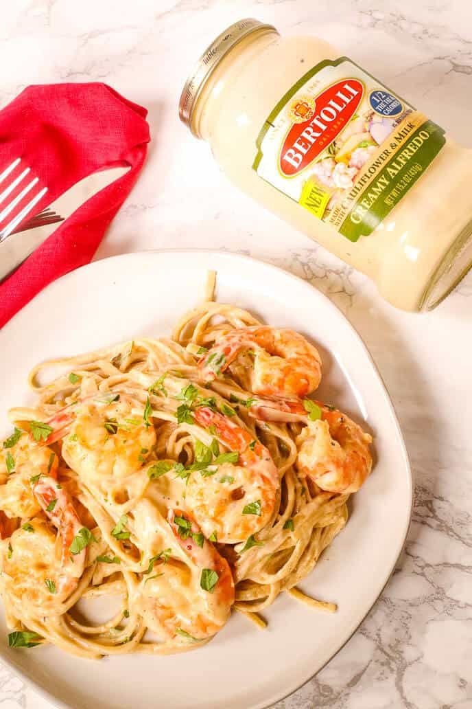 pasta with shrimp and parmesan cheese on a white plate next to a bottle of mayonnaise