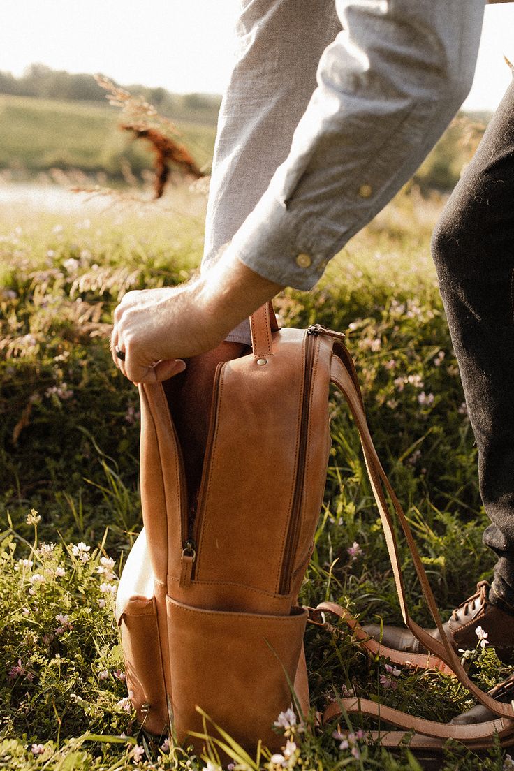 a person standing in the grass with a brown bag