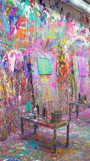 an artist's studio with colorful paint on the walls and tables in front of it