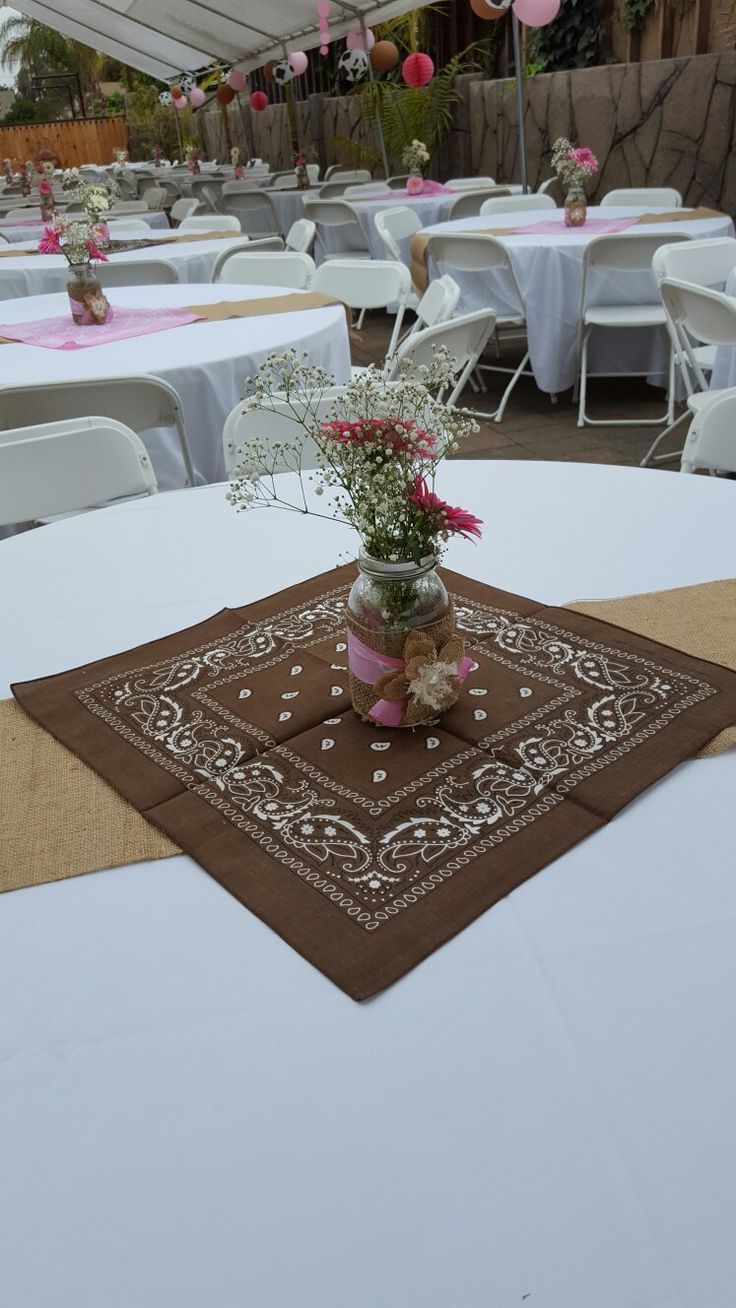 the table is set up with white linens and pink flowers in mason jars on top