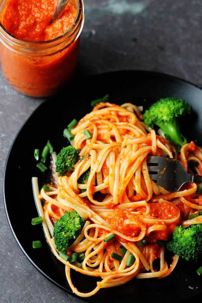 a black plate topped with pasta and broccoli next to a jar of sauce