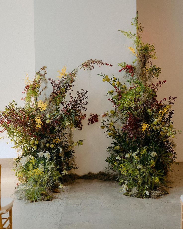 two floral arrangements are arranged on the floor in front of a white wall and chairs