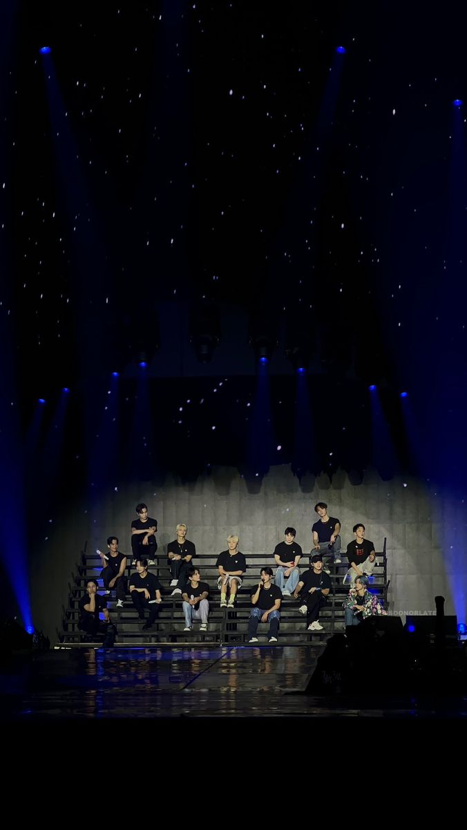 a group of people sitting on top of a stage under blue lights in the dark