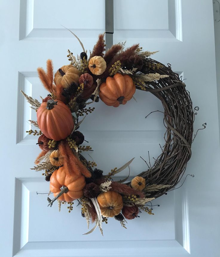 a wreath with pumpkins and gourds is hanging on the front door,