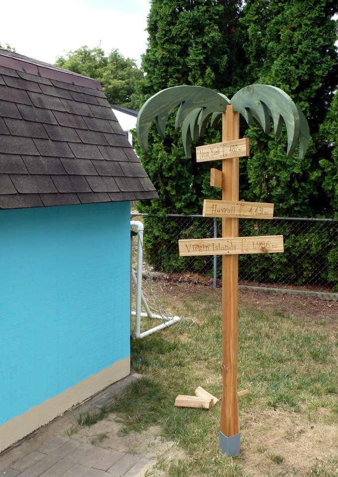 a wooden pole with several signs attached to it in front of a blue wall and fence