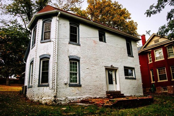 an old white brick house sitting in the middle of a field next to two red houses