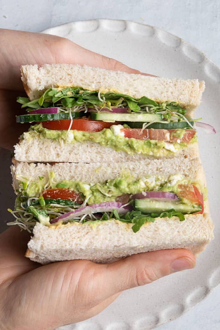 a hand holding a sandwich with lettuce, tomato and other vegetables on it