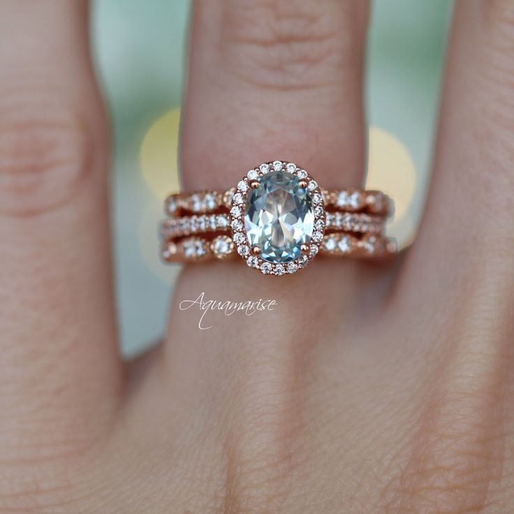 a woman's hand with two wedding bands and an aquamarine colored stone ring