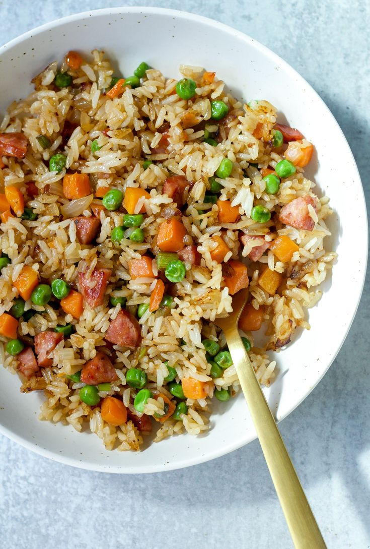 a white bowl filled with rice and vegetables next to a wooden spoon on top of a table