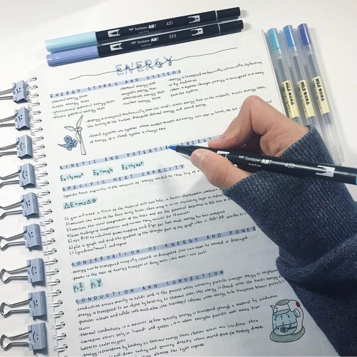 a person holding a pen in front of a paper with writing on it and two other pens