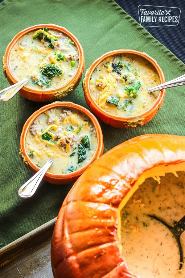 four pumpkin bowls filled with soup on top of a green cloth next to a jack - o'- lantern