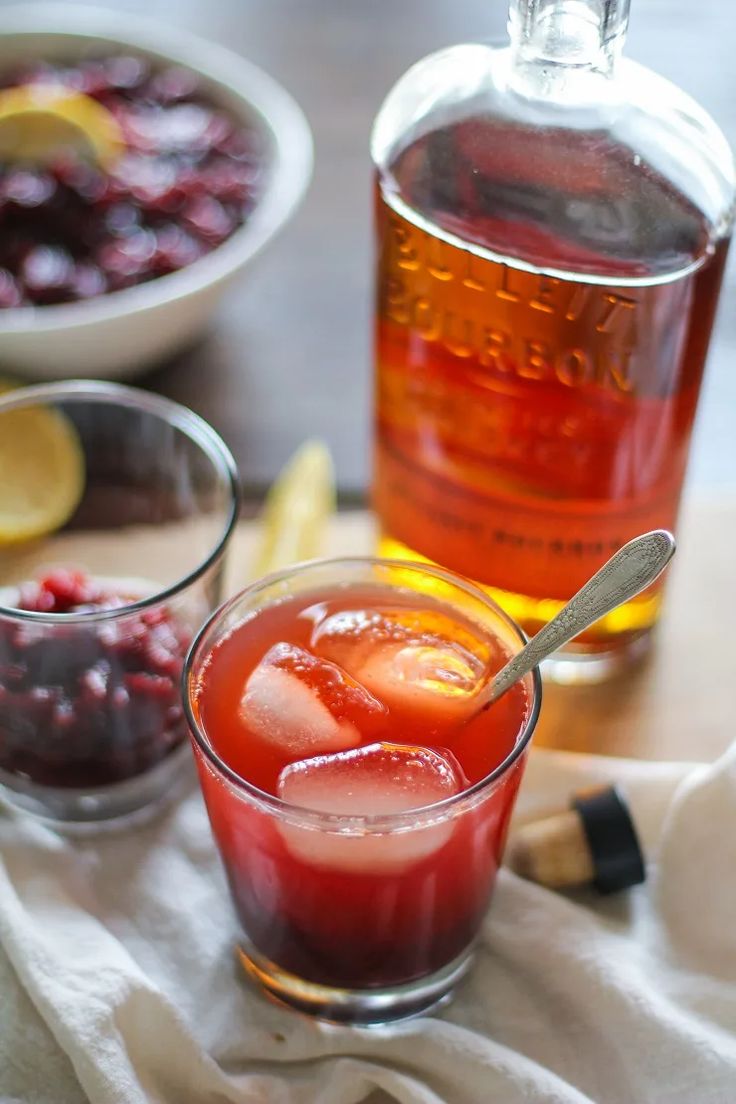 a glass filled with liquid next to a bowl of berries and a bottle of alcohol