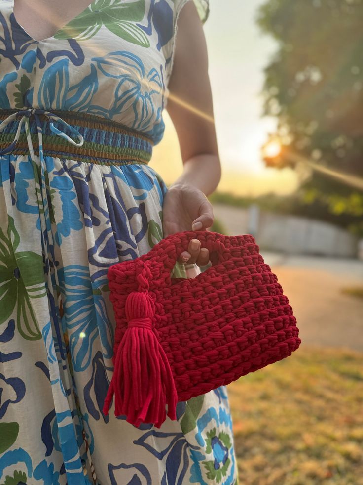 a woman in a dress holding a red crocheted purse with a tassel