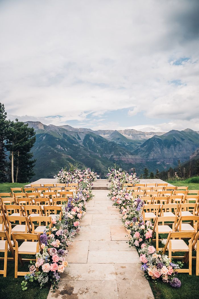 an outdoor ceremony set up with wooden chairs and flowers on the aisle, mountains in the background