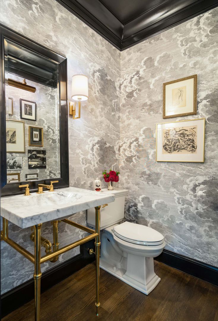 a white toilet sitting next to a sink in a bathroom under a large mirror and framed pictures