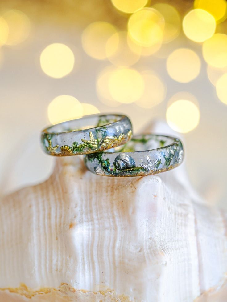 Dive into the beauty of the ocean with our unique resin ring, perfect for sea lovers. Each piece is handcrafted, delicately encapsulating the essence of the beach in a clear light blue tone. Authentic beach sand and tiny moss pieces mimic floating seaweed in crystal-clear waters, while shiny metal embellishments shaped like shells, conchs, and starfish add a touch of elegance and fantasy. This resin ring is perfect for stacking! It's smooth all the way around and it is so comfortable to wear.  A Ocean-inspired Promise Ring, Handmade Ocean-inspired Resin Jewelry, Handmade Ocean-inspired Rings, Moss Ring, Tiny Shells, Ocean Ring, Starfish Jewelry, Mermaid Core, Metal Embellishments