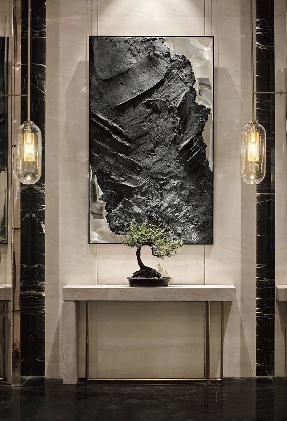 a black and white art piece hanging on the wall above a table with a bonsai tree in it