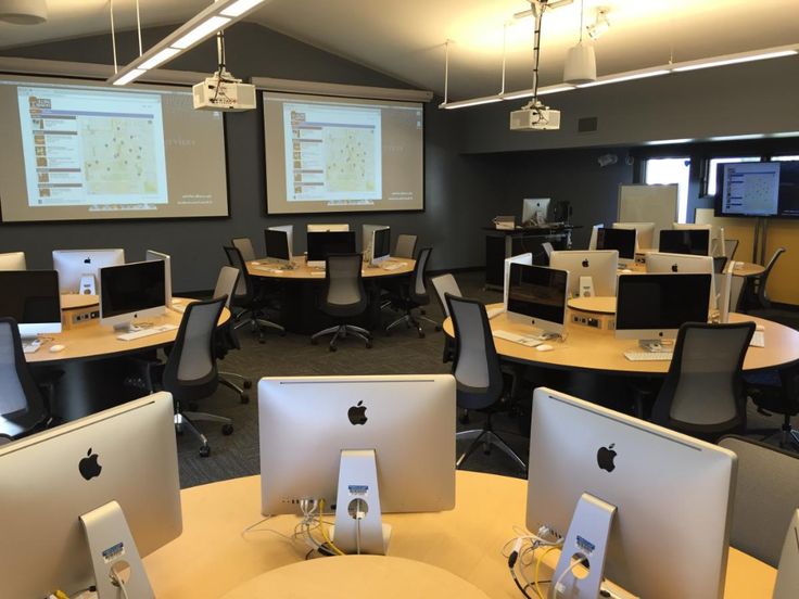 an office with multiple computers and monitors on the desks in front of two large screens