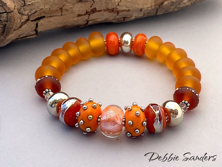 an orange and silver beaded bracelet sitting on top of a piece of driftwood