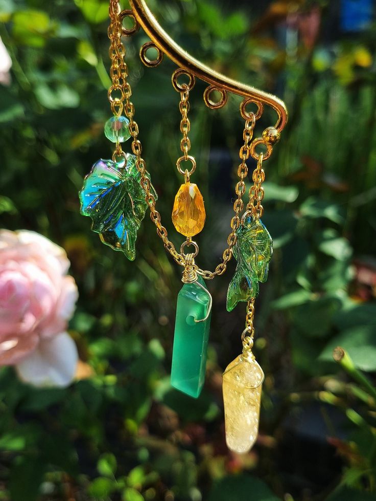 The handmade crystal ear cuff features delicate dangle chains, shimmering green agate and citrine crystals, beads, and ivy leaf charms, this piece is perfect for anyone who loves nature and fantasy. The golden color adds a touch of elegance and sophistication, while the wooden fairy theme adds a playful and whimsical touch. My video instruction on HOW to wear my ear cuff (Insta Reel Video) https://bit.ly/3QkUp4Y See more of my ear cuffs and earrings - https://etsy.me/3SxnsEo If you want a custom request shoot us a message. We can make these crystal crowns and combs with any of the crystals we have available. Handmade Fairy Style Dangle Jewelry, Handmade Fairy Dangle Jewelry, Bohemian Citrine Jewelry For Jewelry Making, Bohemian Citrine For Jewelry Making, Fantasy Style Single Ear Cuff As Gift, Fairycore Gold Dangle Jewelry, Handmade Ethereal Dangle Jewelry, Ethereal Handmade Dangle Jewelry, Handmade Fairycore Ear Cuff As Gift