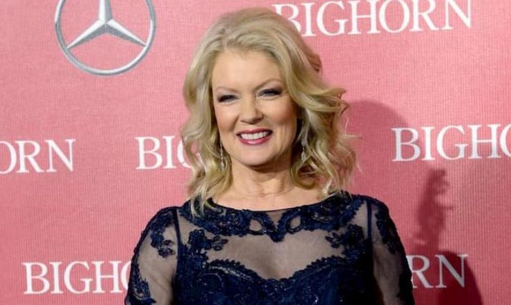 a woman standing in front of a red carpet wearing a black dress and smiling at the camera