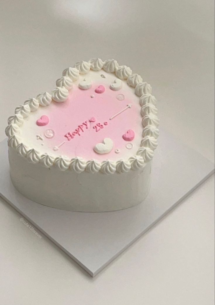 a heart shaped cake with white frosting and pink icing on it's side