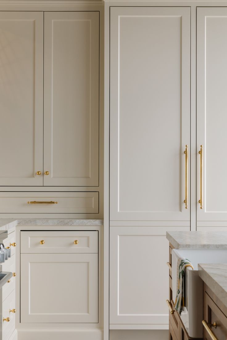 a kitchen with white cabinets and gold pulls on the door handles, marble counter tops