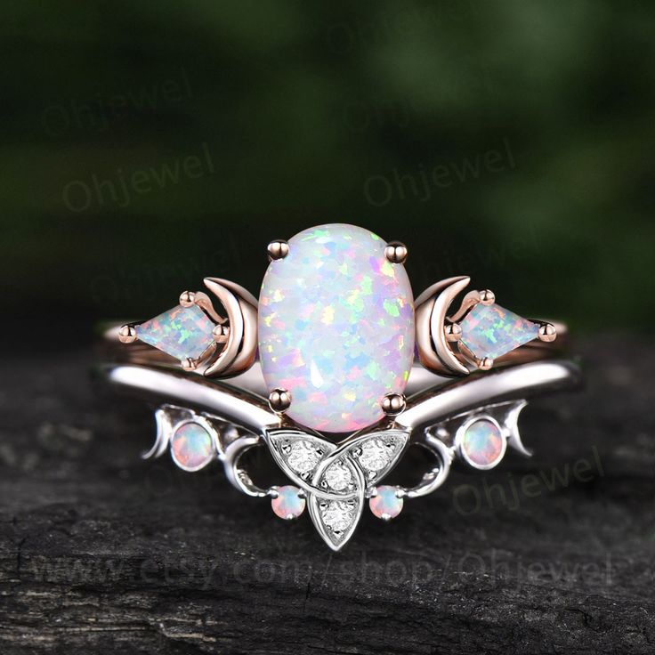 an opalite and diamond ring sitting on top of a piece of wood with leaves