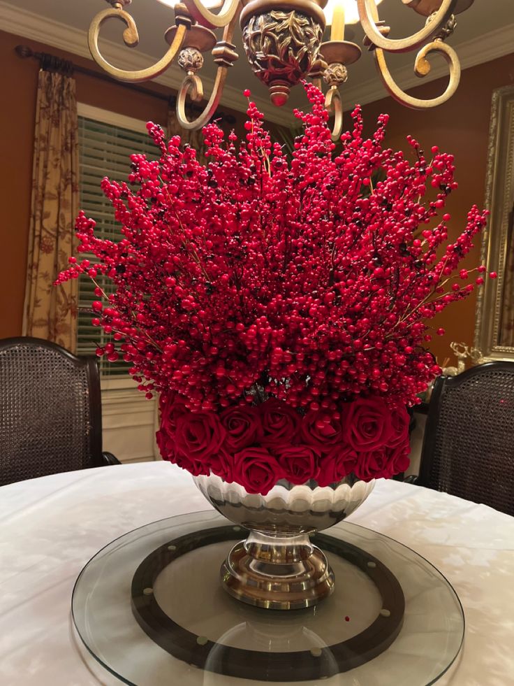 a vase filled with red flowers sitting on top of a glass tablecloth covered dining room table