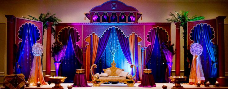 a stage set up for a wedding with purple, orange and blue decorations on it