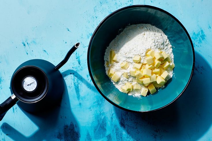 a bowl filled with flour next to a measuring cup on top of a blue table