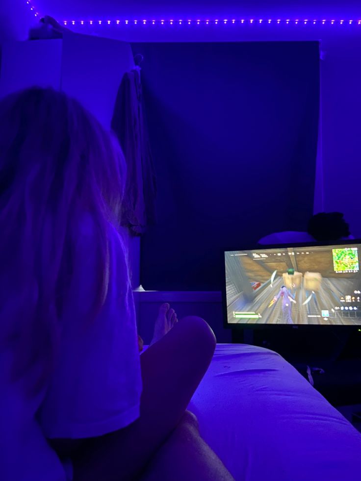 a woman sitting in front of a tv playing a game on the nintendo wii at night