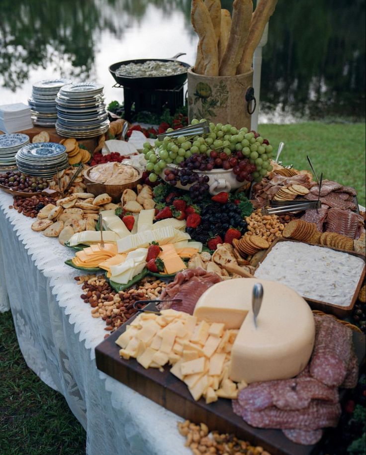 an assortment of cheeses and meats on a table with water in the background