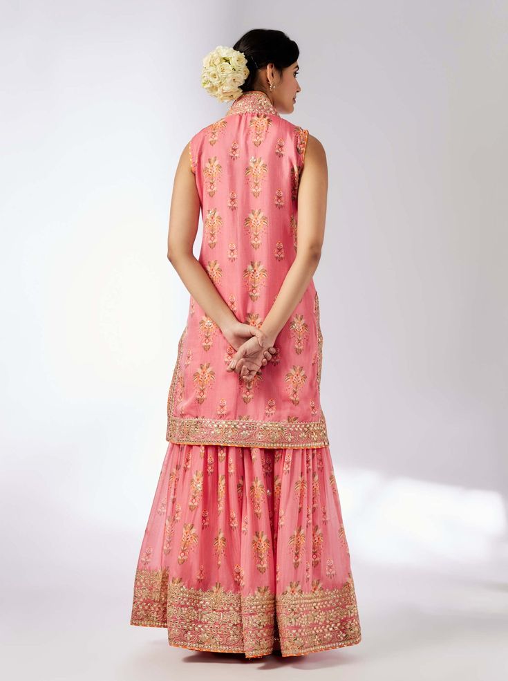 This pretty ensemble of floral jaal, with intricate border embroidery. The sleeveless kurta is embellished down the front and tried with a smart pleated magzi to finish the neckline and armhole. The flowing sharara bottom with gota embroidery still has a lot of flounce and flow. Sleeveless Sharara With Gota Work For Festivals, Festival Sleeveless Sharara With Gota Work, Sleeveless Chanderi Dress With Mirror Work, Sleeveless Resham Embroidery Sharara For Festivals, Sleeveless Anarkali Sharara For Festive Season, Sleeveless Chanderi Traditional Wear With Chikankari Embroidery, Sleeveless Chanderi Kurta For Wedding, Designer Sleeveless Kurta With Mirror Work, Sleeveless Festive Palazzo Set For Diwali