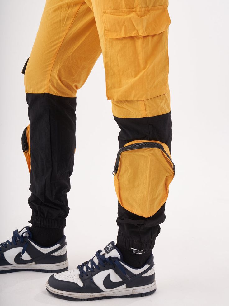 Double-color yellow and black joggers with four functional cargo pockets on the knees and elastic ankles. FEATURES Slim Fit Made up of 95% Cotton and 5% Elastane Jogger comfort Drawstring waist SIZE GUIDE Model's height and weight: 6"1 feet & 180 lbs. (185 cm & 82 kg ) Model wears size: L Streetwear Nylon Cargo Pants With Functional Pockets, Outdoor Nylon Techwear Joggers, Sporty Outdoor Joggers With Hip Pockets, Streetwear Nylon Parachute Pants With Functional Pockets, Sporty Nylon Cargo Pants With Functional Pockets, Sporty Parachute Pants With Hip Pockets For Streetwear, Nylon Parachute Pants With Functional Pockets For Streetwear, Sporty Cargo Style Joggers For Streetwear, Techwear Joggers With Cargo Pockets For Outdoor