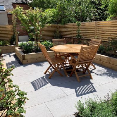 a wooden table sitting on top of a patio next to a lush green garden filled with flowers