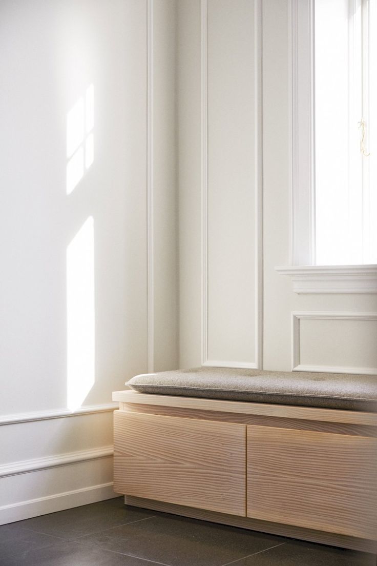 a wooden bench sitting in front of a window next to a white wall and floor