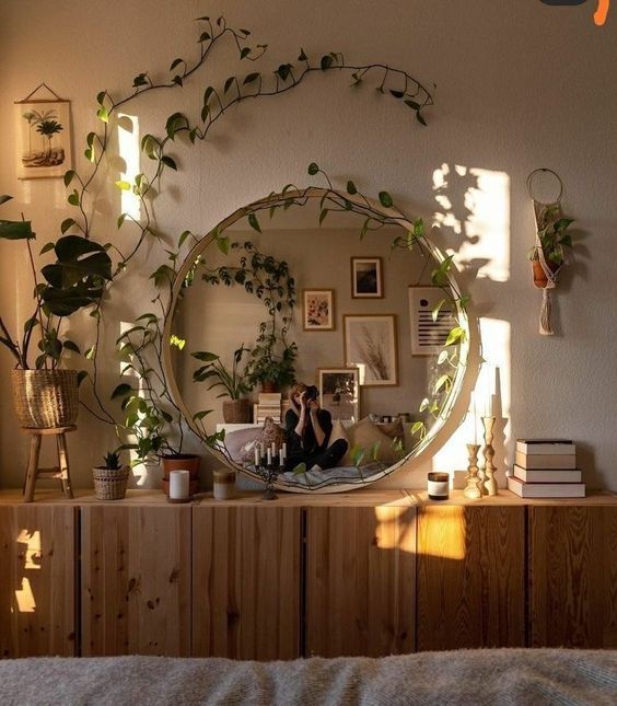 a mirror sitting on top of a wooden dresser next to a plant filled wall mounted above it