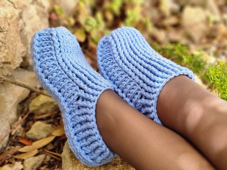 a woman's legs wearing blue knitted slippers on top of leaves and rocks