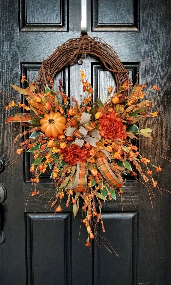 the red rustic rose fall wreath is hanging on a front door with an orange pumpkin