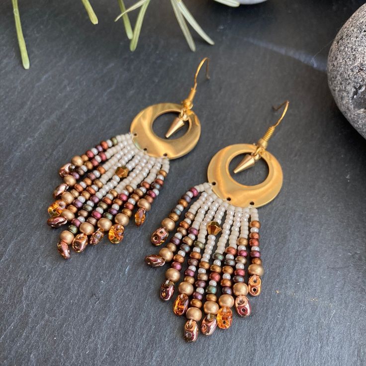 two pairs of beaded earrings sitting on top of a black table next to a potted plant