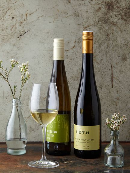 three bottles and two glasses of wine sitting on a table next to vases with flowers