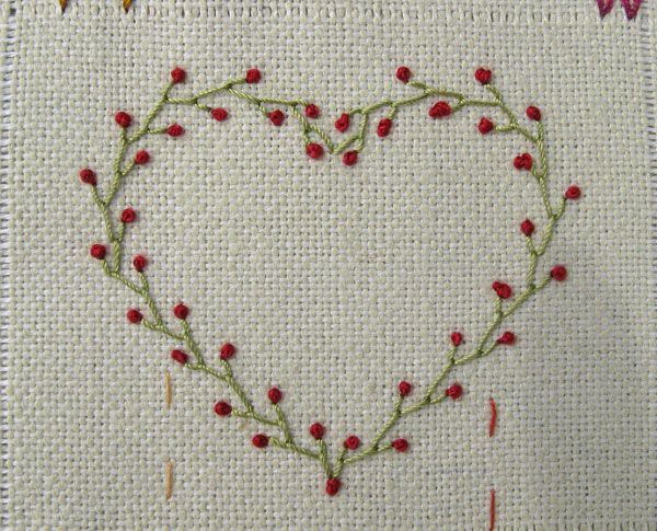 a cross stitched heart with red flowers on the side and two hearts in the middle