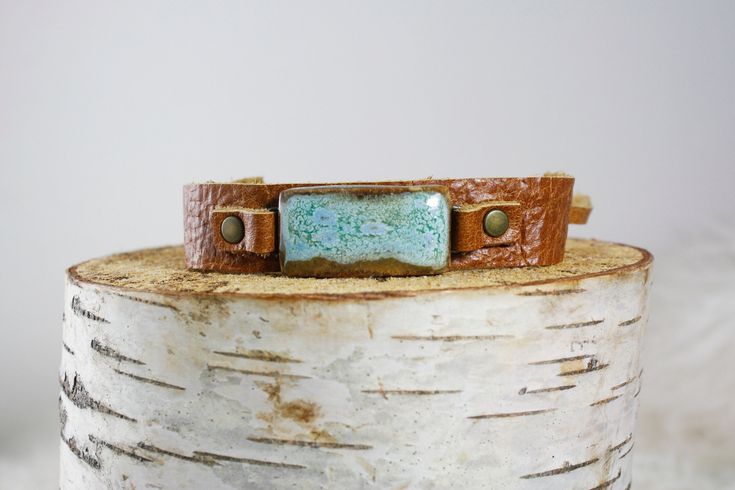 Ceramic lagoon tie bracelet. Saddle leather. One size fits all, unisex. You've arrived at Dandy Outlet! This handcrafted ceramic piece of jewelry is handmade and one-of-a-kind, and the piece pictured is the piece you will receive. As with outlet shopping, each item is imperfect. It may have a drip or a hole, or the glaze may not have turned out as intended. Your win! Outlet prices are 25-50% off regular store and website prices.  Outlet pieces are final sale only, and stock is limited. Please as Unique Adjustable Bracelet With Leather Strap, Adjustable Leather Strap Bracelet, Artisan Jewelry With Leather Strap For Gift, Rustic Leather Strap Jewelry Gift, Rustic Jewelry With Leather Strap For Gift, Rustic Leather Bracelet With Patina For Gift, Rustic Leather Bracelet With Patina As Gift, Handmade Leather Bracelet With Waxed Cord For Gifts, Handmade Adjustable Rectangular Leather Bracelet