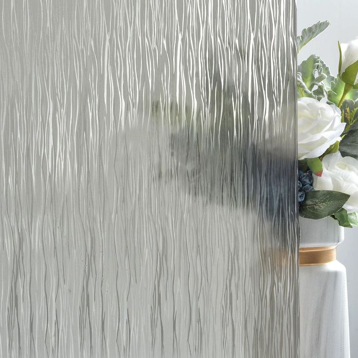 a vase with white flowers in front of a frosted glass window that has wavy lines on it