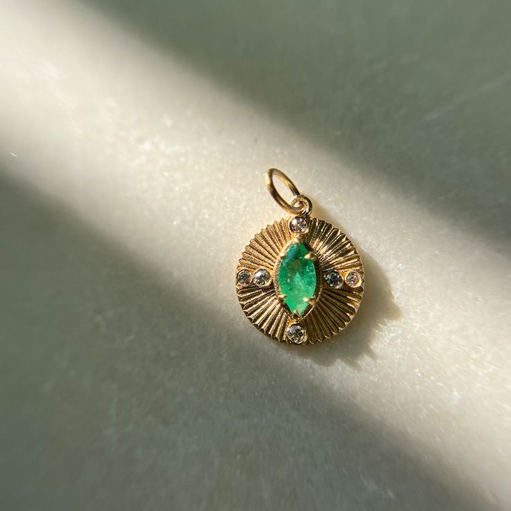 The Mini Damona charm is a fluted coin shaped pendant that features a center marquise cut emerald and accenting bezel set diamonds. Inspired by ancient treasure and compasses this charm mixes modern and vintage details for a unique symbolic heirloom piece. Center marquise emerald measures 6mmx3mm and diamonds measure 1.3mm, 1.2mm, and 1mm for a total diamond carat weight of .04 Cts. Heirloom Marquise Emerald Jewelry, Timeless Green Pendant Jewelry, Elegant Green Jewelry With Coin Pendant, Heirloom Style Marquise May Birthstone Jewelry, Heirloom Marquise May Birthstone Jewelry, Ancient Treasure, Ethical Engagement Ring, Vintage Details, Stackable Wedding Bands